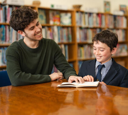 IB student helping younger student with reading in the library as part of CAS
