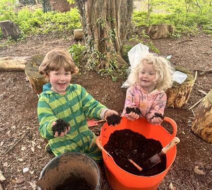 Two young children playing in the mud at Sidcot Forest School