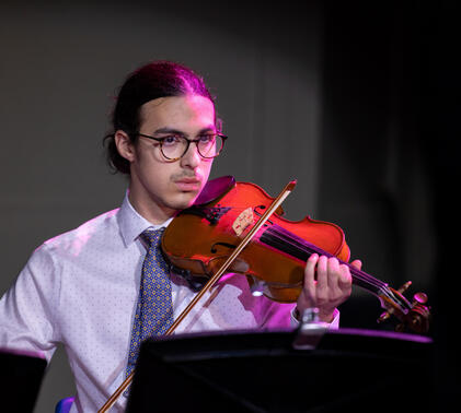 Sidcot Head Student, Pip, holding his violin under a purple spotlight