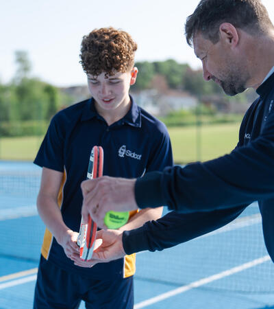 Sidcot student being shown how to play tennis by Sidcot school teacher