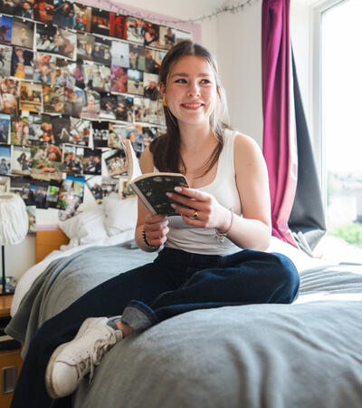 Girl in boarding sat on bed reading book